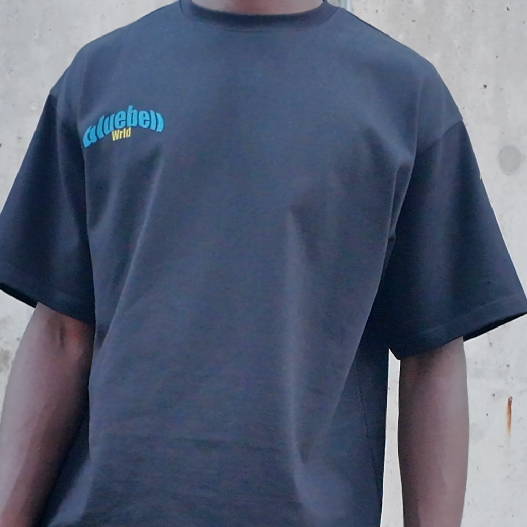 model wearing a black t-shirt with "bluebell wrld" text on a concrete wall background